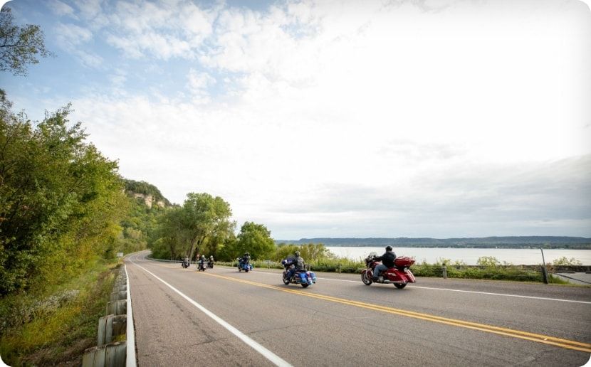 A group of motorcyclists driving along the river.