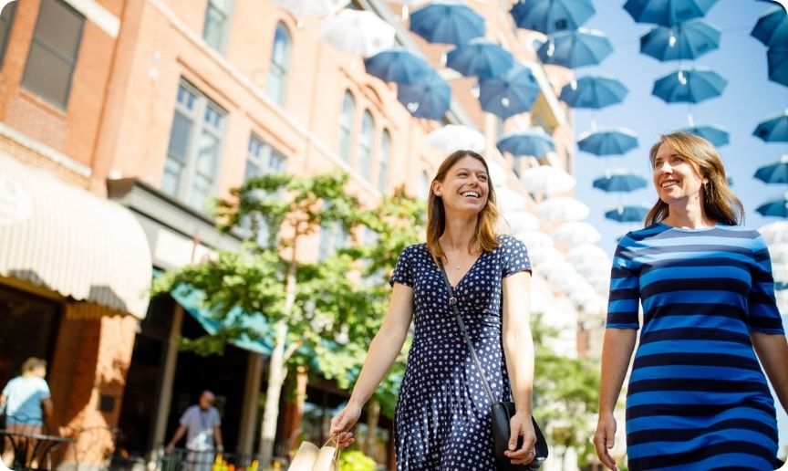 Two women walking underneath a colorful canopy of umbrellas. 