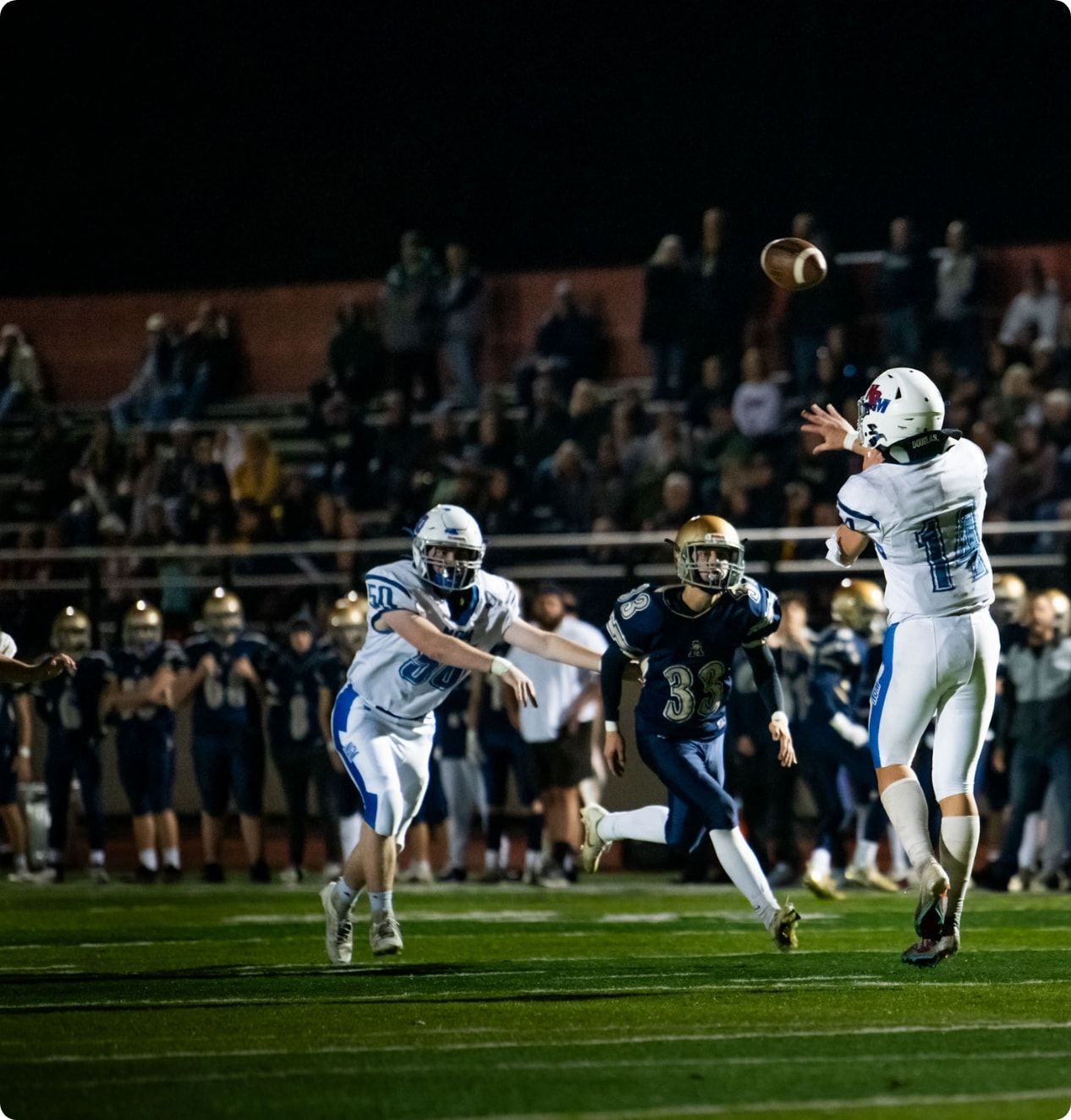 A football player jumping up to receive the ball while two other players run toward him. 