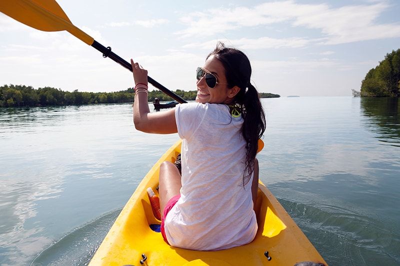 A woman sitting in the front seat of a kayak on a lake. 