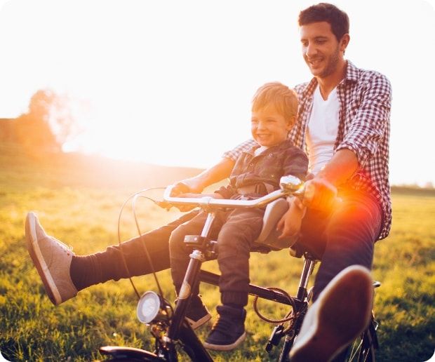 A man riding a bicycle while a young boy sits between him and the handlebars. 